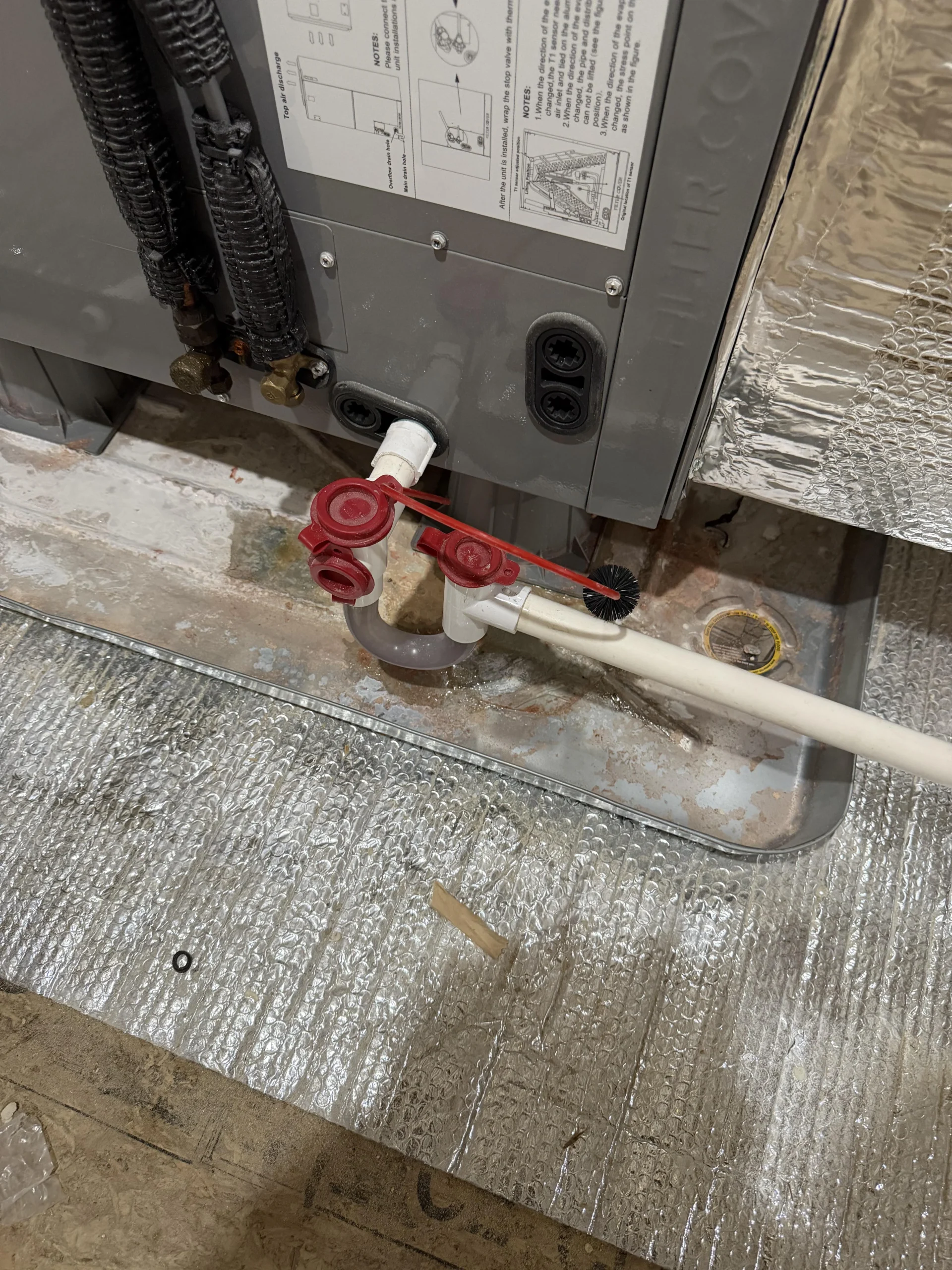 HVAC air handler with white drain piping and a condensate trap in an attic area